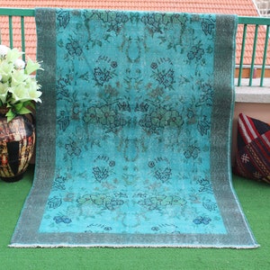 Pu&ograve; includere: Un tappeto vintage blu turchese con un motivo floreale. Il tappeto ha un aspetto sbiadito ed &egrave; fatto di lana. Il tappeto &egrave; su una superficie di erba verde.