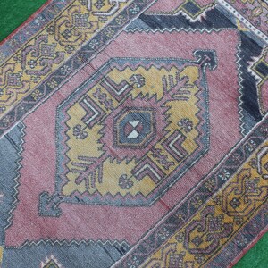 K&ouml;nnte beinhalten: Ein Vintage-Teppich mit einem geometrischen Muster in Rosa, Gelb und Blau. Der Teppich hat einen verblassten, abgenutzten Look und ist aus Wolle.