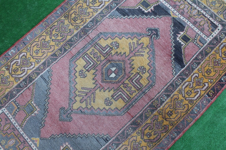 K&ouml;nnte beinhalten: Ein Vintage-Teppich mit einem geometrischen Muster in Rosa, Gelb und Blau. Der Teppich hat einen verblassten, abgenutzten Look und ist aus Wolle.