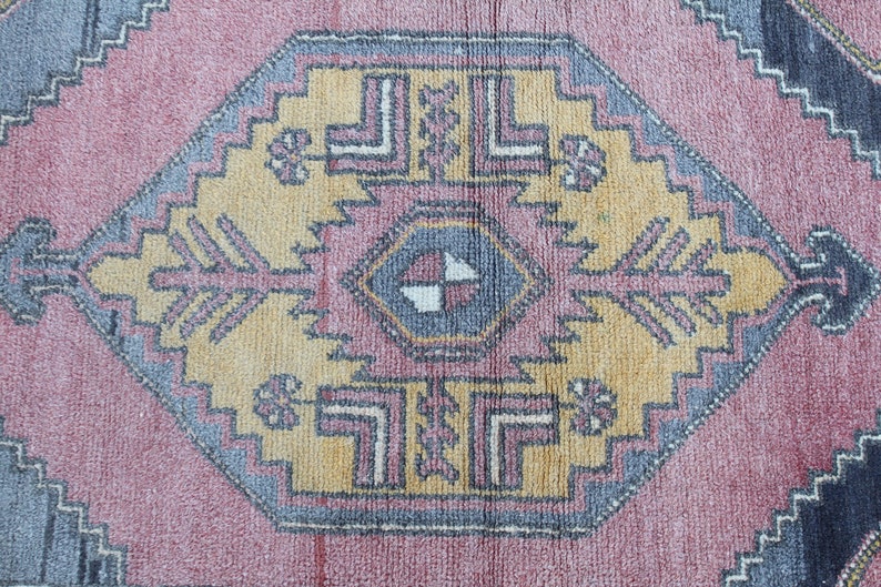 K&ouml;nnte beinhalten: Ein Vintage-Teppich mit einem geometrischen Muster in den Farben Rosa, Gelb, Blau und Grau. Der Teppich hat eine zentrale Diamantform mit einem kleineren Diamanten im Inneren. Der Teppich ist abgenutzt und verblasst, was ihm einen rustikalen Look verleiht.