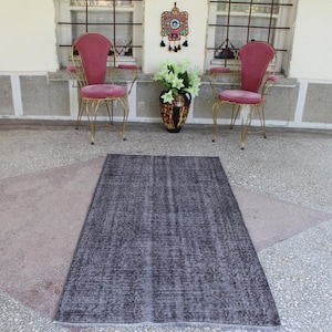 May include: A dark gray area rug with a subtle textured pattern. The rug is laid out on a light gray tiled floor in front of two pink velvet chairs with gold metal frames.