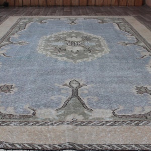 May include: A vintage rug with a light blue center and a beige border. The rug has a floral pattern in the center and a geometric pattern in the border.
