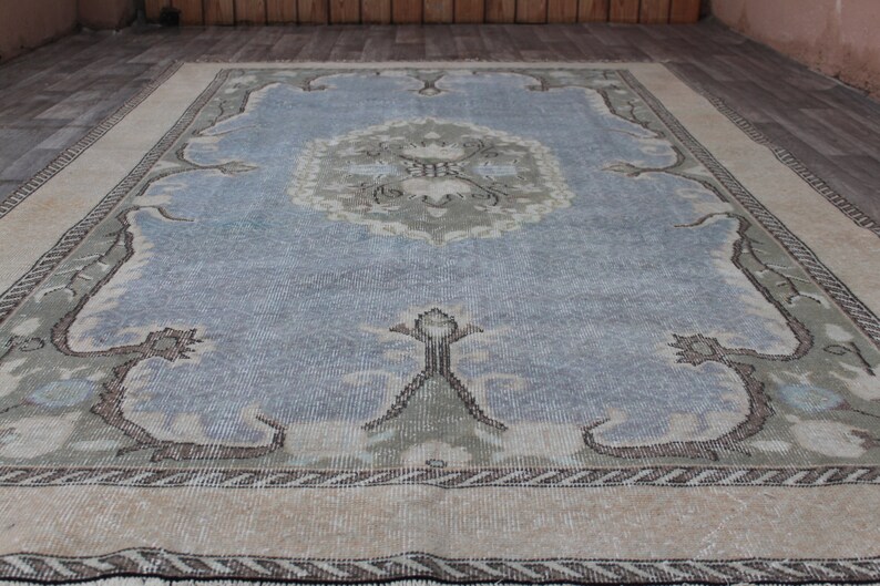May include: A vintage rug with a light blue center and a beige border. The rug has a floral pattern in the center and a geometric pattern in the border.