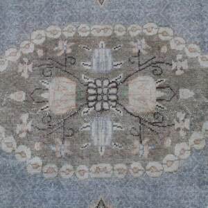 May include: A vintage rug with a light blue background and a central oval design. The oval features a floral pattern in shades of beige, brown, and white.