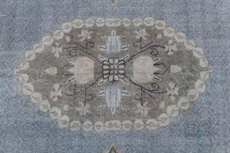 May include: A vintage rug with a light blue background and a central oval design. The oval features a floral pattern in shades of beige, brown, and white.