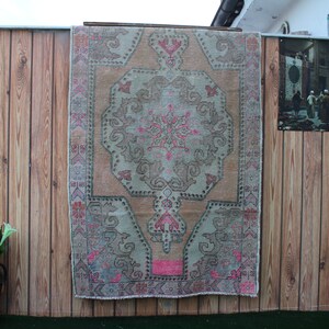 May include: A vintage rug with a light pink, beige, and gray color scheme. The rug has a traditional Persian design with a central medallion and intricate floral patterns. The rug is hanging on a wooden wall.