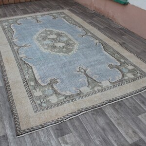 May include: A vintage rug with a light blue center and a cream-colored border. The rug has a floral pattern in shades of green and brown.
