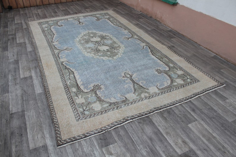 May include: A vintage rug with a light blue center and a cream-colored border. The rug has a floral pattern in shades of green and brown.