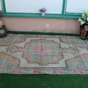Puede incluir: Una alfombra vintage con un fondo beige claro y un medall&oacute;n central en tonos verdes, rosas y naranjas. La alfombra tiene un aspecto descolorido, desgastado y un patr&oacute;n geom&eacute;trico.