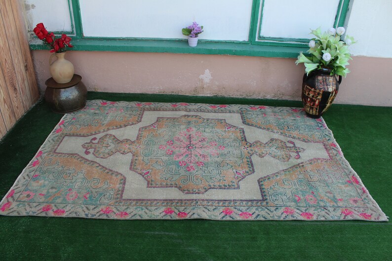 Puede incluir: Una alfombra vintage con un fondo beige claro y un medall&oacute;n central en tonos verdes, rosas y naranjas. La alfombra tiene un aspecto descolorido, desgastado y un patr&oacute;n geom&eacute;trico.