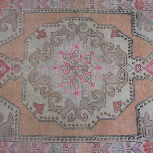 May include: A vintage rug with a faded pink and brown color scheme. The rug features a central medallion with intricate floral designs and a repeating pattern of geometric shapes.
