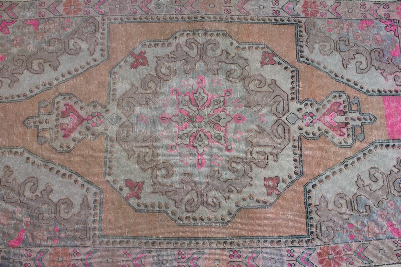 May include: A vintage rug with a faded pink and brown color scheme. The rug features a central medallion with intricate floral designs and a repeating pattern of geometric shapes.