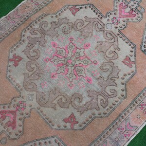May include: A vintage Turkish rug with a faded pink and brown color scheme. The rug features a central medallion with intricate floral designs and a geometric border.