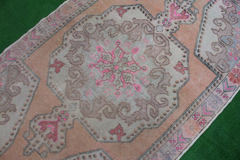 May include: A vintage Turkish rug with a faded pink and brown color scheme. The rug features a central medallion with intricate floral designs and a geometric border.