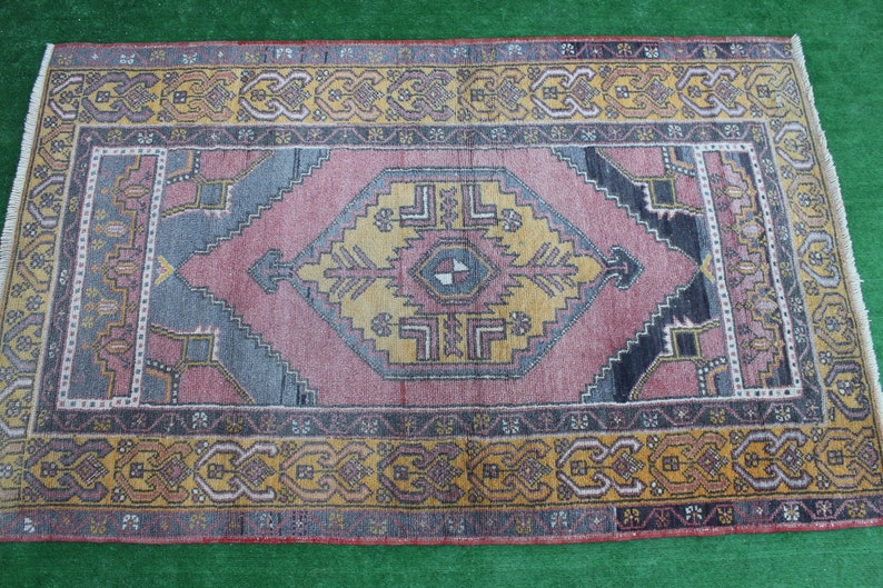 K&ouml;nnte beinhalten: Ein Vintage-Teppich mit einem geometrischen Muster in Rosa, Blau und Gelb. Der Teppich hat einen dunkelbraunen Rand mit komplizierten Designs.