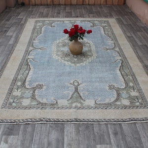 May include: A light blue rug with a beige border and a floral pattern. A terracotta vase with red roses sits in the center of the rug.
