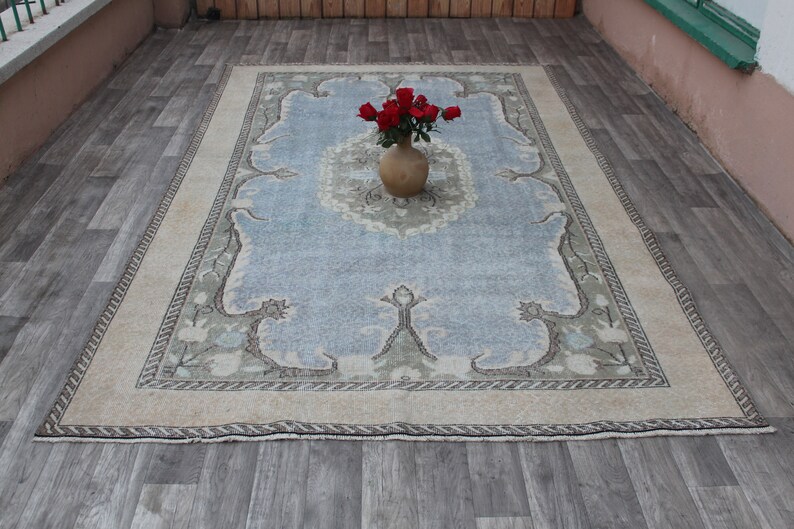 May include: A light blue rug with a beige border and a floral pattern. A terracotta vase with red roses sits in the center of the rug.