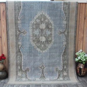May include: A vintage rug with a light blue background and a beige border. The rug has a central medallion with a floral design in shades of beige and gray.