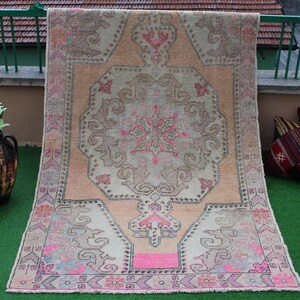 May include: A vintage Turkish rug with a light pink and cream color scheme. The rug has a central medallion with a floral design and a geometric border.