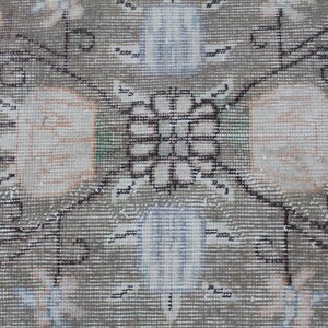 May include: A close-up of a beige rug with a detailed floral pattern in black and white. The center of the rug features a symmetrical design with a square shape and a floral motif.