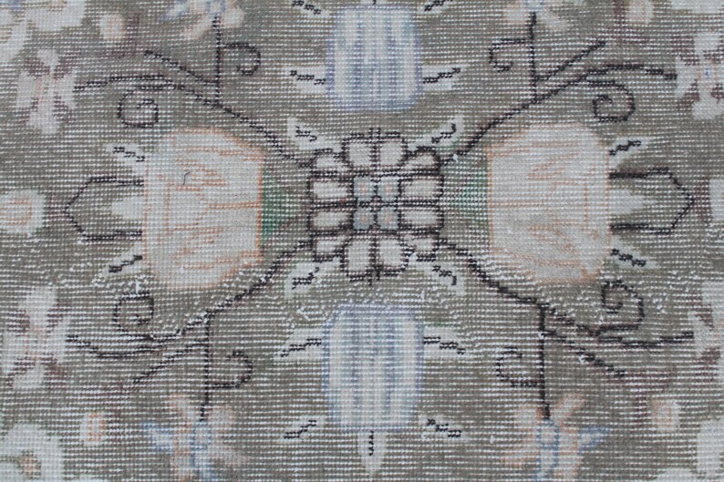 May include: A close-up of a beige rug with a detailed floral pattern in black and white. The center of the rug features a symmetrical design with a square shape and a floral motif.