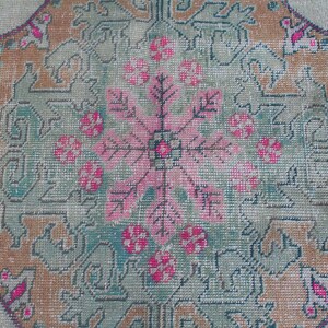 Puede incluir: Primer plano de una alfombra vintage con un dise&ntilde;o floral central en tonos rosa, verde y marr&oacute;n. La alfombra tiene un aspecto descolorido y desgastado, con un fondo blanco.