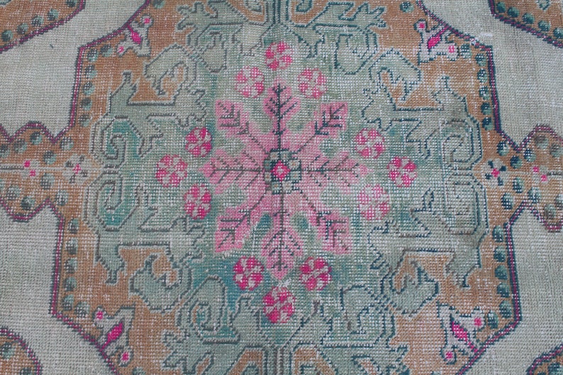 Puede incluir: Primer plano de una alfombra vintage con un dise&ntilde;o floral central en tonos rosa, verde y marr&oacute;n. La alfombra tiene un aspecto descolorido y desgastado, con un fondo blanco.
