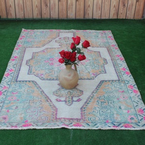 Puede incluir: Una alfombra blanca y rosa con estampado con un arreglo floral en un jarr&oacute;n de cer&aacute;mica marr&oacute;n en la parte superior. La alfombra est&aacute; sobre una superficie de c&eacute;sped artificial verde.