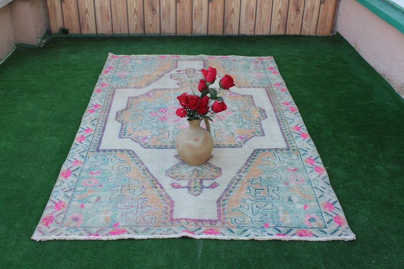 Puede incluir: Una alfombra blanca y rosa con estampado con un arreglo floral en un jarr&oacute;n de cer&aacute;mica marr&oacute;n en la parte superior. La alfombra est&aacute; sobre una superficie de c&eacute;sped artificial verde.