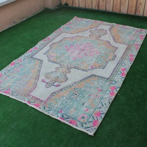 Puede incluir: Una alfombra turca vintage con fondo blanco y un colorido patr&oacute;n floral en tonos rosa, azul y naranja. La alfombra tiene un aspecto desgastado y es perfecta para a&ntilde;adir un toque de estilo bohemio a cualquier habitaci&oacute;n.