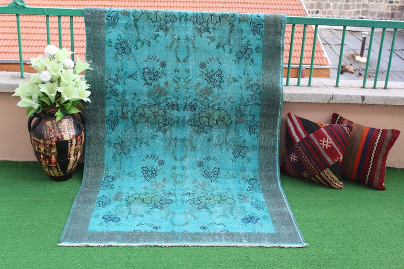 Pu&ograve; includere: Un tappeto vintage blu turchese con un motivo floreale. Il tappeto ha un aspetto sbiadito ed &egrave; fatto di lana. Il tappeto &egrave; su una superficie di erba verde.