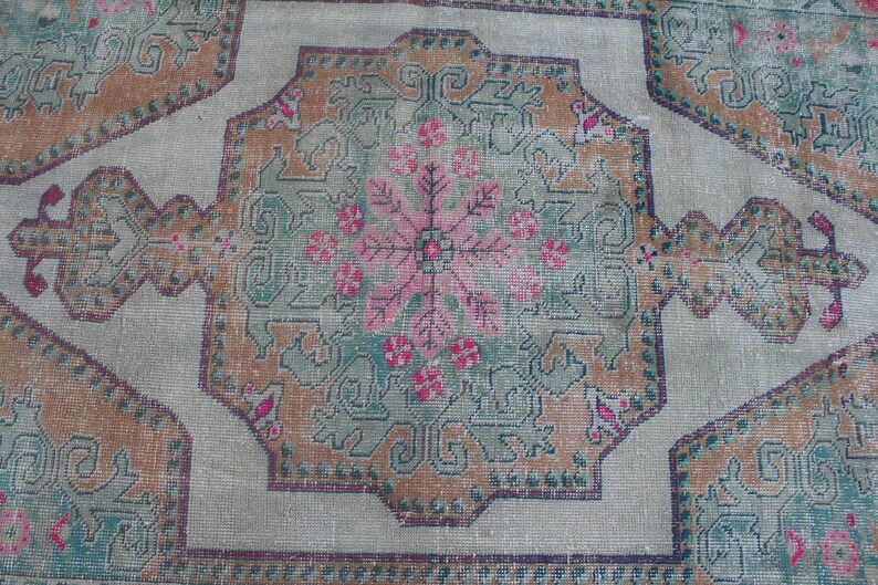 Puede incluir: Una alfombra vintage con un dise&ntilde;o central de medall&oacute;n que presenta un patr&oacute;n floral en tonos de rosa, verde y marr&oacute;n. La alfombra tiene un fondo beige claro y un borde con un patr&oacute;n geom&eacute;trico repetitivo.