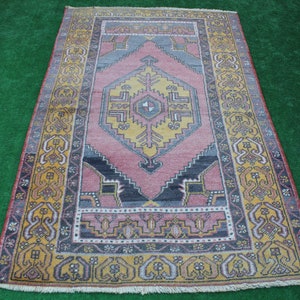 K&ouml;nnte beinhalten: Ein Vintage-Teppich mit einem geometrischen Muster in Rosa, Gelb und Blau. Der Teppich hat einen Fransenrand und einen gelben Rand.