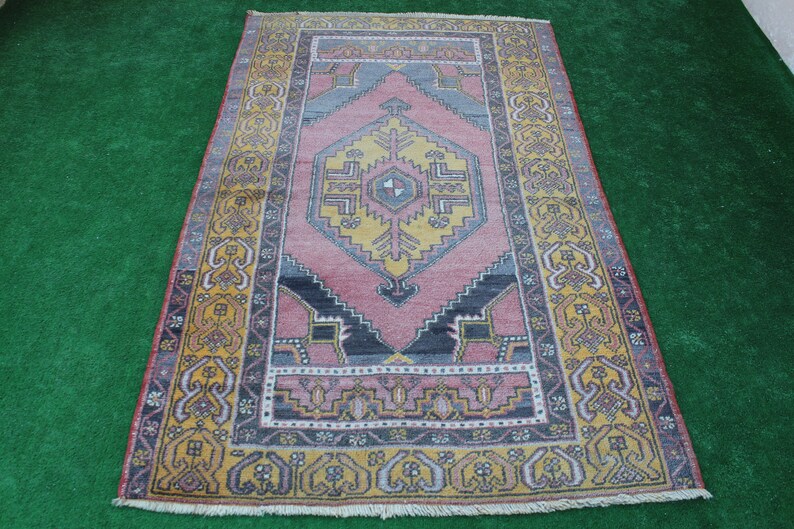 K&ouml;nnte beinhalten: Ein Vintage-Teppich mit einem geometrischen Muster in Rosa, Gelb und Blau. Der Teppich hat einen Fransenrand und einen gelben Rand.