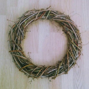 May include: A brown twig wreath with a natural, rustic look. The wreath is made of interwoven branches and twigs, creating a circular shape.