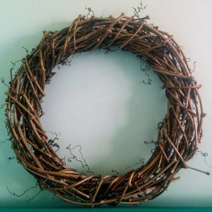 May include: A brown grapevine wreath with a natural, rustic look. The wreath is made of interwoven branches and vines, creating a circular shape.