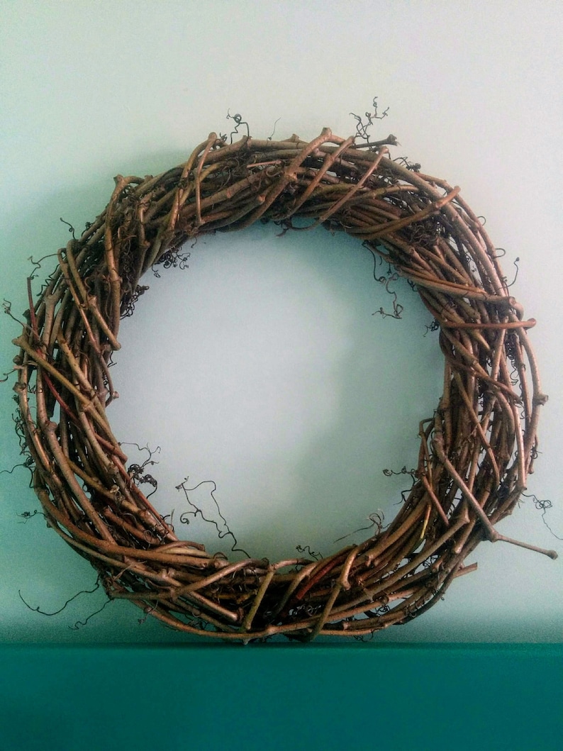 May include: A brown grapevine wreath with a natural, rustic look. The wreath is made of interwoven branches and vines, creating a circular shape.