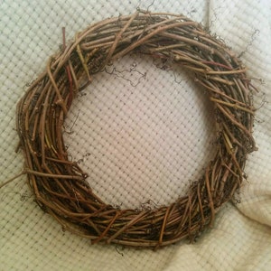 May include: A brown twig wreath, made of natural branches, is displayed on a white fabric background.