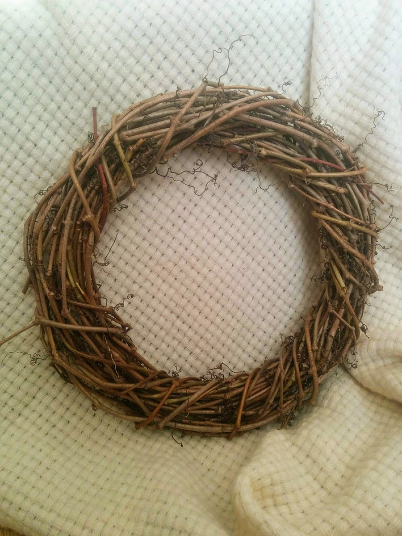 May include: A brown twig wreath, made of natural branches, is displayed on a white fabric background.