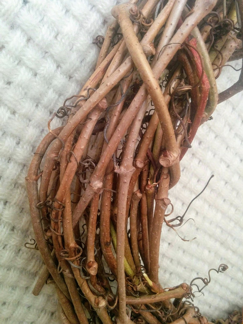 May include: A close-up of a brown grapevine wreath. The vines are intertwined and have a natural, rustic look.