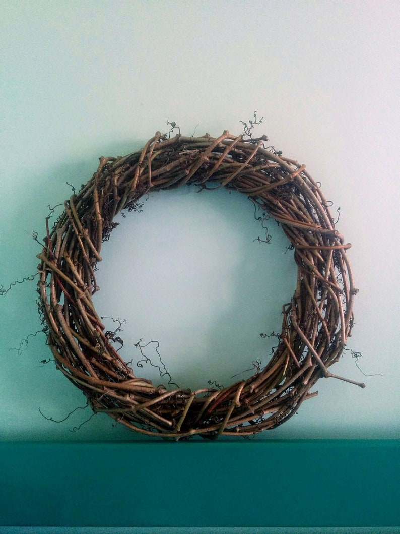 May include: A brown grapevine wreath with a natural, rustic look. The wreath is made of intertwined branches and twigs, creating a circular shape.
