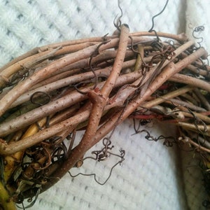 May include: A close-up of a brown grapevine wreath. The wreath is made from natural grapevine branches and is ideal for decorating a home or adding a rustic touch to a space.