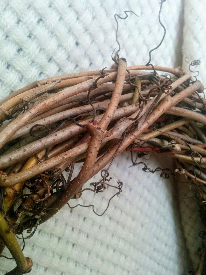 May include: A close-up of a brown grapevine wreath. The wreath is made from natural grapevine branches and is ideal for decorating a home or adding a rustic touch to a space.