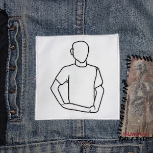 Peut inclure: Un écusson blanc cousu sur une veste en jean avec un dessin au trait noir et blanc d'une personne les bras croisés. L'écusson est entouré d'autres écussons, dont un avec le mot "HUMAN" dessus.