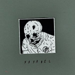 May include: A square embroidered patch featuring a white skull and upper torso graphic on a black background. The design includes a circular emblem on the chest area. Below the patch, the text XA XA BEL is printed in black on the surface.