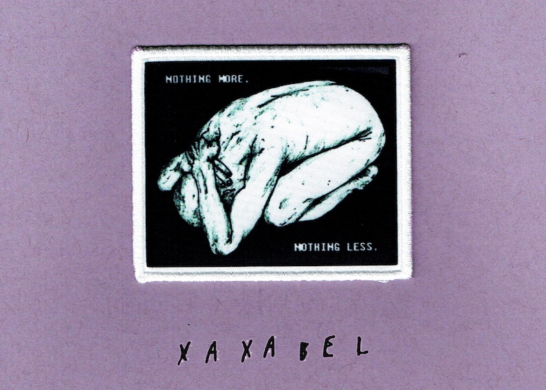 May include: A rectangular embroidered patch with a white border featuring a black background and a white illustration of a figure curled in a fetal position. The text "NOTHING MORE." appears in the top left and "NOTHING LESS." in the bottom right.