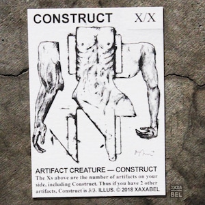 May include: A rectangular white card featuring a black ink sketch of a fragmented human torso and arms. The text CONSTRUCT X/X appears at the top, with ARTIFACT CREATURE - CONSTRUCT and descriptive game rules printed at the bottom, dated 2018 XAXABEL.