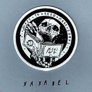 May include: A circular embroidered patch with a white border featuring a black and white illustration of a skeleton reading an open book. The text "TRY TO READ MORE BOOKS" is printed in a circular arc along the top edge of the black background.