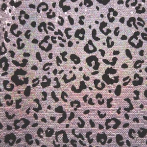 May include: A close-up of a fabric with a black leopard print pattern on a iridescent pink background. The fabric is covered in sequins.