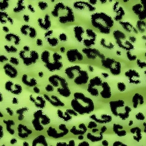 May include: Green fabric with a black leopard print. The fabric has a shiny, glittery texture.